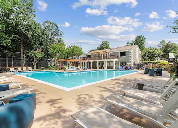 A large swimming pool with sun loungers and a building in the background.