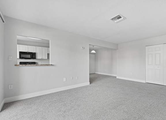 A spacious living room with a grey carpet and white walls.