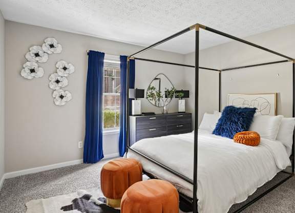 A bedroom with a four poster bed and a window with blue curtains.