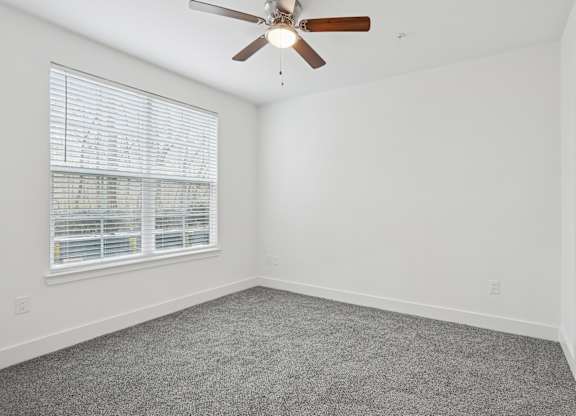 A room with a ceiling fan and a window with blinds.