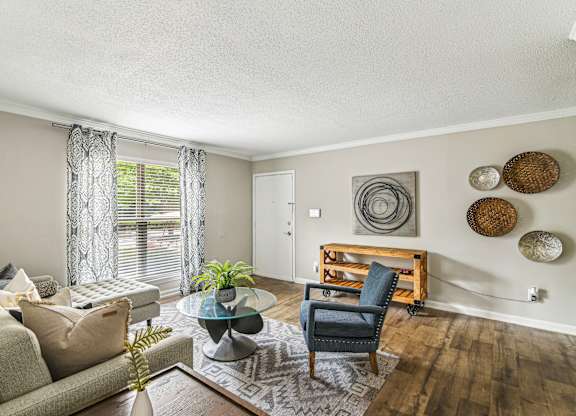 A living room with a grey couch, a blue chair, a glass coffee table, and a wooden shelf with baskets on it.