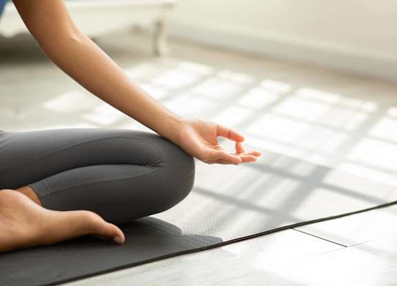 A person is sitting cross-legged on a yoga mat with their hands in a prayer position.