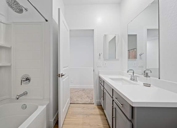 A white bathroom with a tub, sink, and mirror.