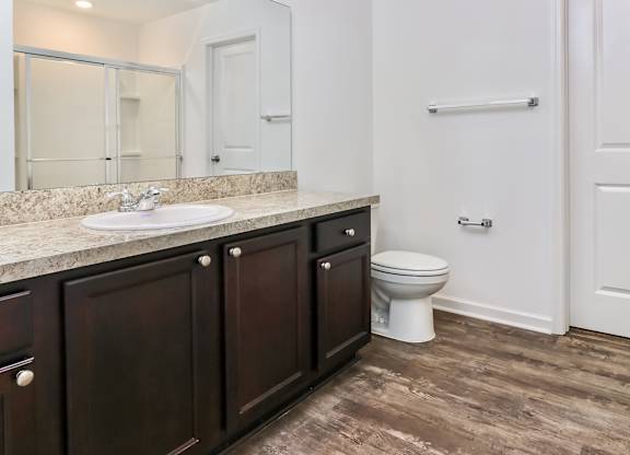 A white toilet sits in a bathroom with dark wood cabinets.