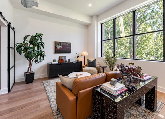 A living room with a brown leather couch, a glass coffee table, and a large window.