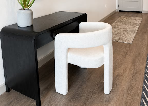 A black desk with a white chair and a round mirror on the wall.