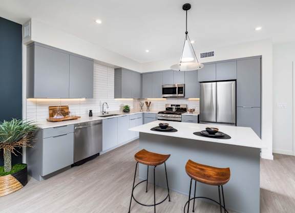A modern kitchen with a bar stool and a hanging light fixture.