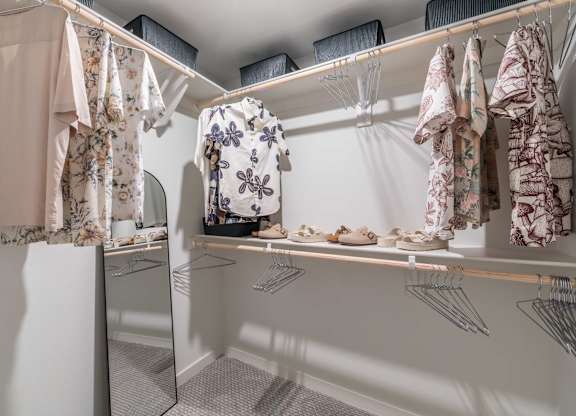 A white closet with clothes hanging and shoes on a shelf.
