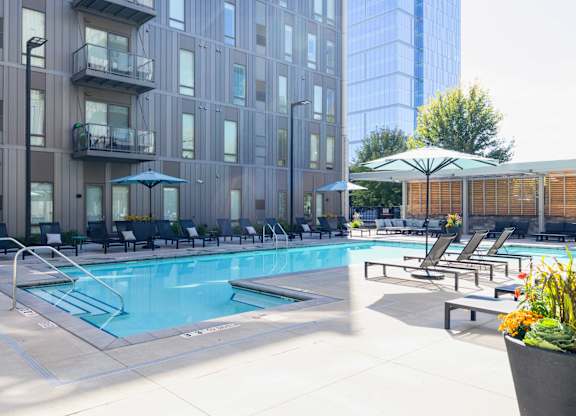 A pool area with chairs and umbrellas in front of a building.