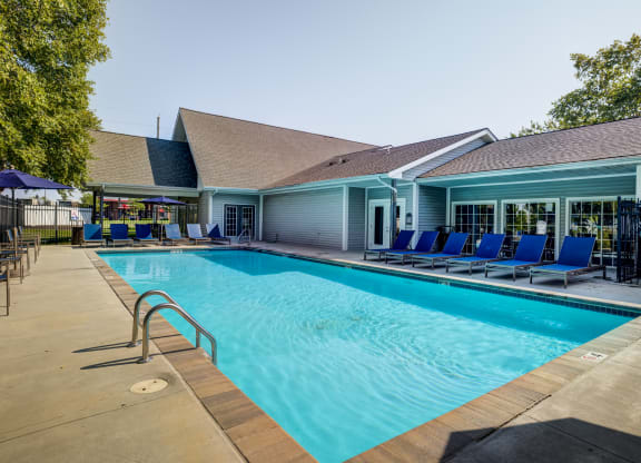 a swimming pool with blue chaise lounge chairs and a building in the background