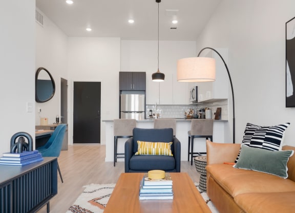 a living area with a couch coffee table and chair and a kitchen in the background