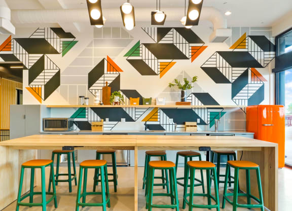 a long wooden table with green and orange stools in front of a white and black wall