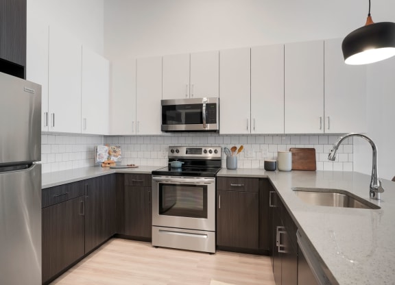 1 Bedroom Apartments In Wheat Ridge, CO - The Parallel - Gourmet Kitchen with White Upper Cabinets and Dark Brown Lower Cabinets, White Tile Backsplash, Quartz Countertops, Stainless Steel Appliances, and Luxury Plank Floors