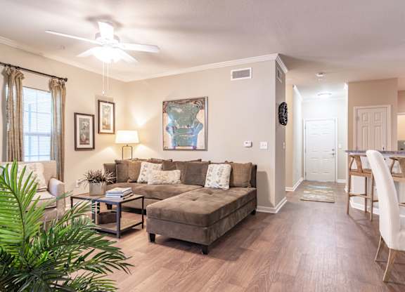 Opelika, AL Apartments – The Crossings of Opelika - a living room with a couch and a table with hardwood floors and a ceiling fan