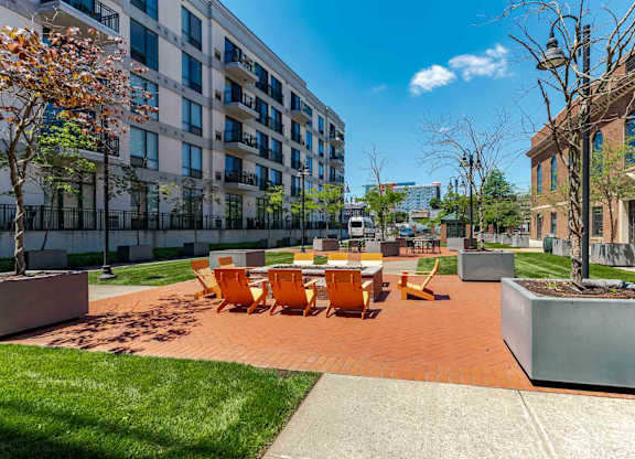 A sunny day at a courtyard with orange chairs and a white table.