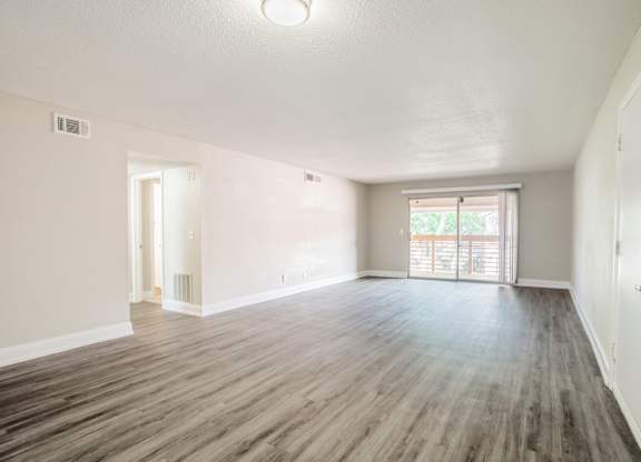 Living room with hardwood-style flooring, large window, and sliding door at Townsend Apartments in Jacksonville near Atlantic Beach, Florida.