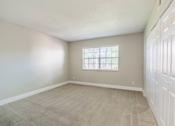 Bright bedroom featuring plush carpet and a large window at Townsend Apartments in Jacksonville near Atlantic Beach, Florida.