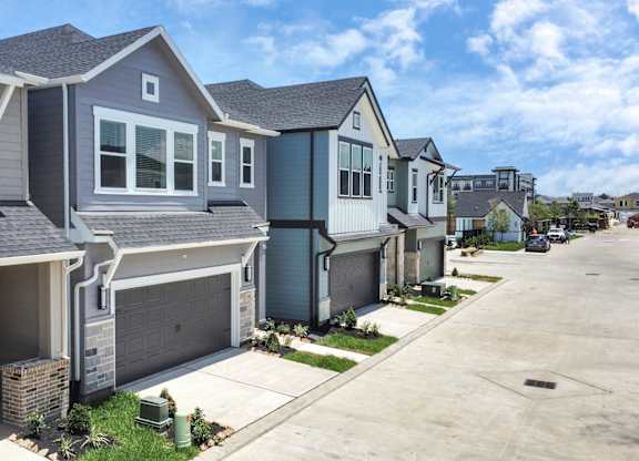 Houses for Rent in Heights, Houston, TX - The Crossings at Timbergrove - A Row of Houses with Attached Garages, a Driveway, and a Green Grass Area.
