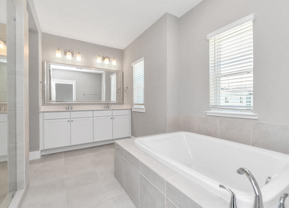Heights, Houston, TX, Homes For Rent - The Crossing at Timbergrove - Bathroom with Bathtub, Tile Flooring, a Double Vanity with White Cabinets, and a Large Mirror.