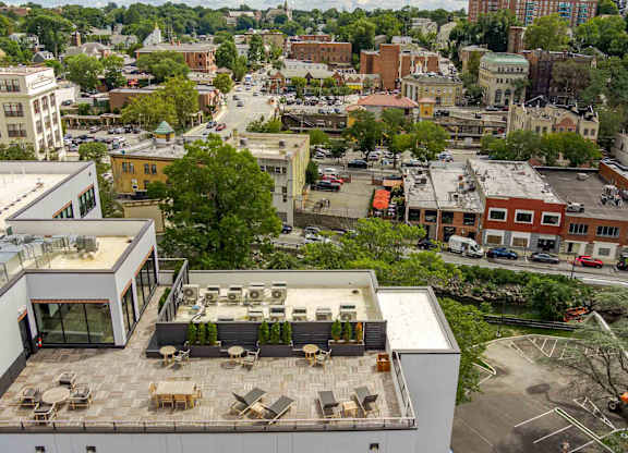 A modern building with a rooftop patio is surrounded by other buildings in a city.