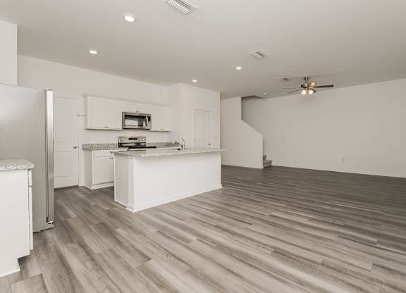 A kitchen with a refrigerator, stove, and wooden floors.