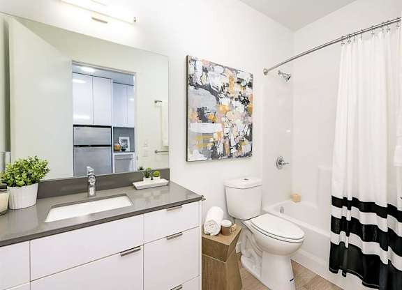 Fremont, WA Apartments - Inspire Fremont - Bathroom with a Bathtub, Granite-Style Sink, and a Large Mirror