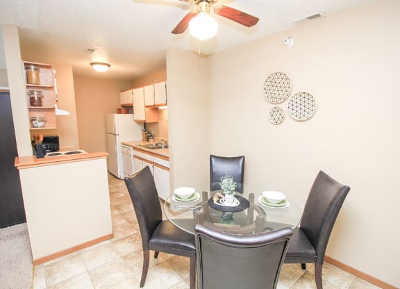 a dining room with a table and chairs and a kitchen in the background
