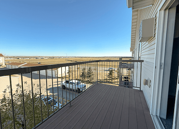 A balcony with a wooden floor and a metal railing overlooking a parking lot.