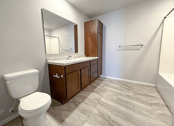 A bathroom with a toilet, sink, and wooden cabinets.