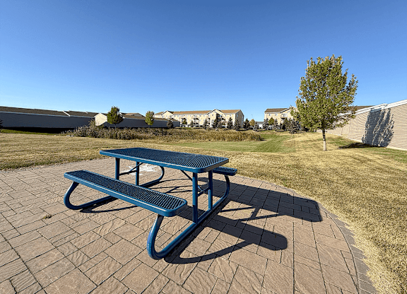 A blue picnic table is in the foreground of a grassy area.
