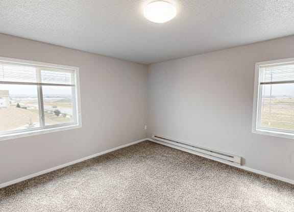 A room with a carpeted floor and two windows.