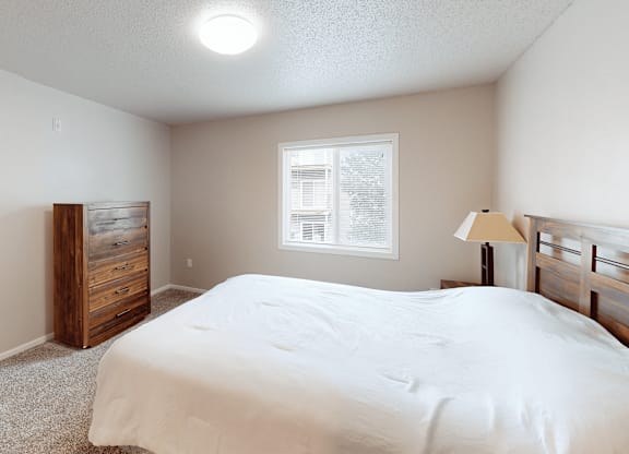 A bedroom with a bed, dresser, and window.