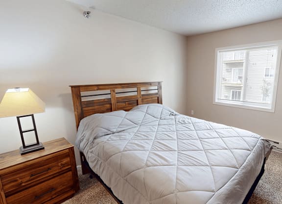 A bedroom with a bed, nightstand, and window.