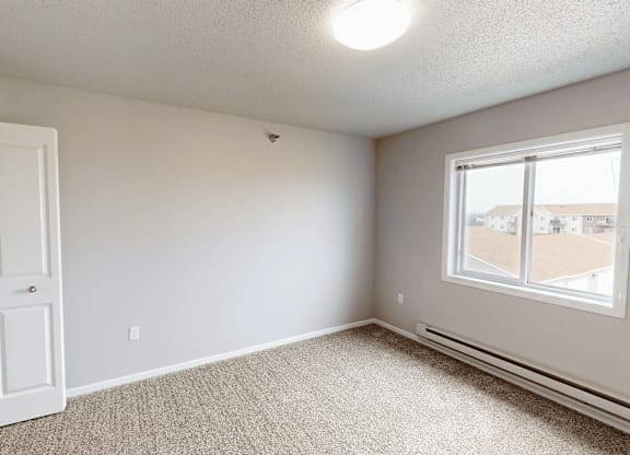 A room with a carpeted floor, a window, and a door.