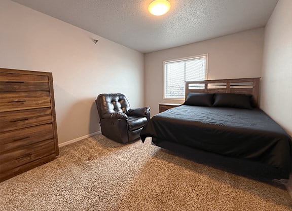 A bedroom with a bed, chair, and dresser.