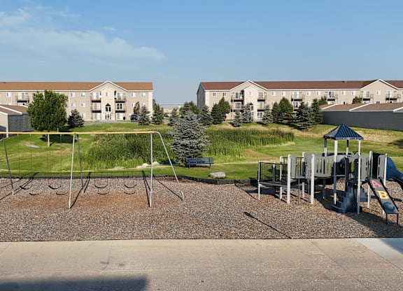 A playground with a slide and swings in front of apartment buildings.