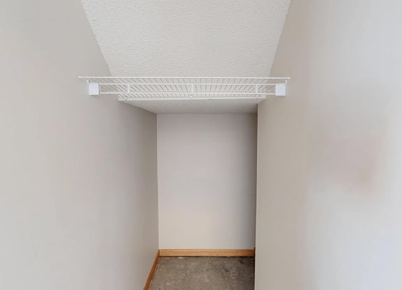 A white wall with a white shelf on top and a brown floor.