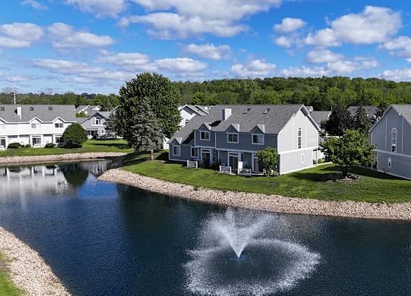 A fountain in the middle of a lake in front of a row of houses.