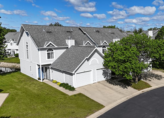 A white house with a grey roof and a tree in front.