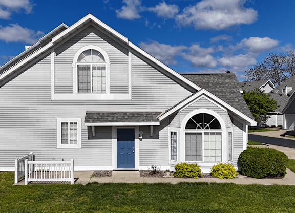 A grey house with a blue door and white windows.