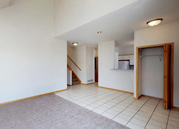 A room with a carpeted floor and a staircase in the background.