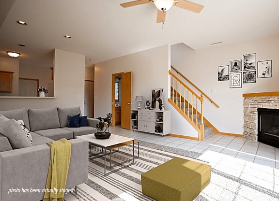 A living room with a grey couch, a yellow ottoman, and a fireplace.