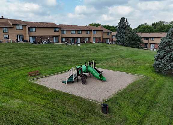 A playground with a green slide and a red bench in front of apartment buildings.
