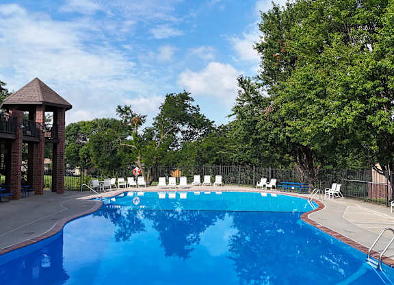 A large blue swimming pool with white lounge chairs and a gazebo in the background.