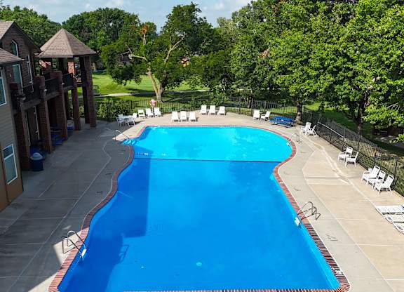 A large blue swimming pool surrounded by trees and a building.