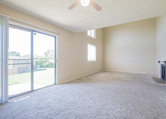 A room with a carpeted floor, a ceiling fan, and a fireplace.