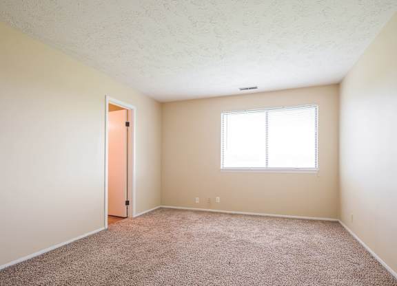 A room with a carpeted floor, a window, and a door.