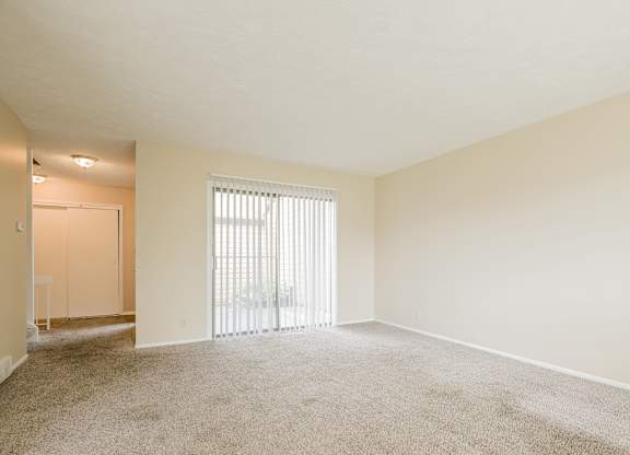 A large, empty room with a carpeted floor and a sliding glass door leading to a balcony.
