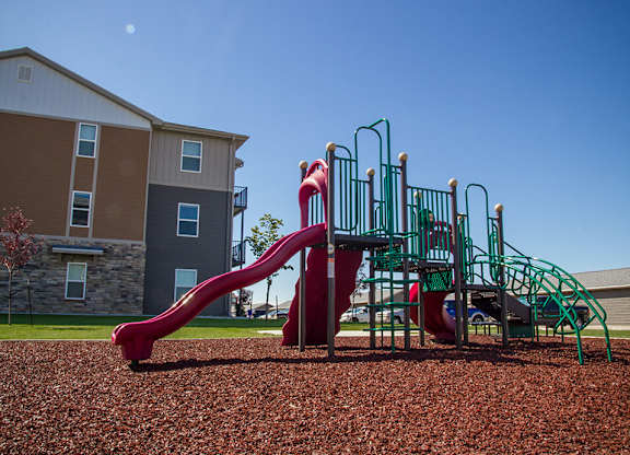 a playground with a slide and climbing equipment in front of an apartment building