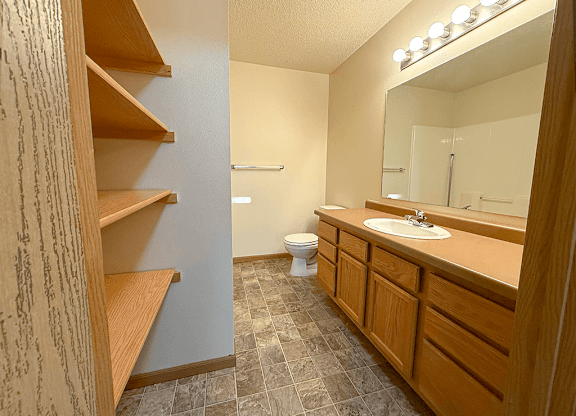 A bathroom with a toilet, sink, and wooden shelves.